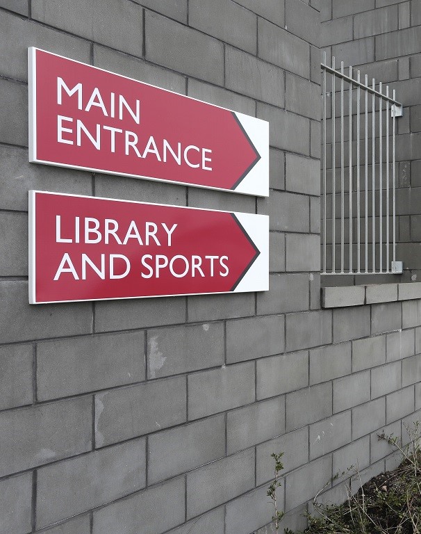 sign design, external wayfinding, white text on red sign tray, panel fitted through brickwork