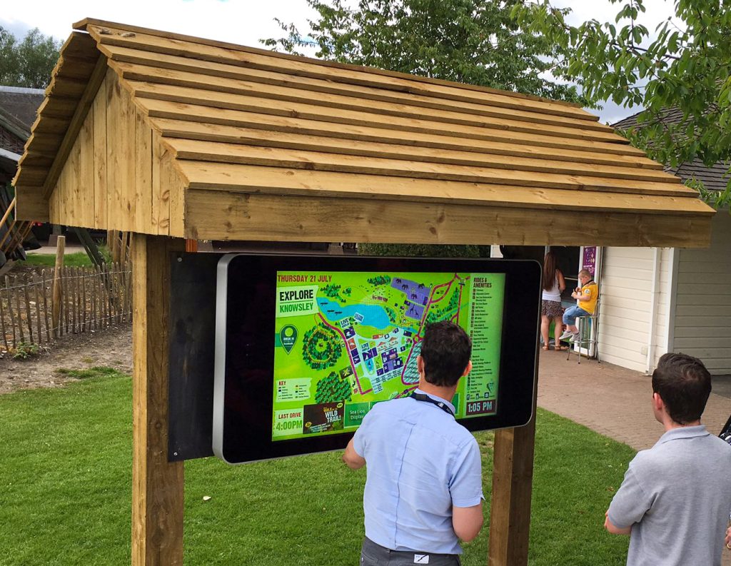 Outdoor digital display housed under a wooden hut. The display shows a map of the park.