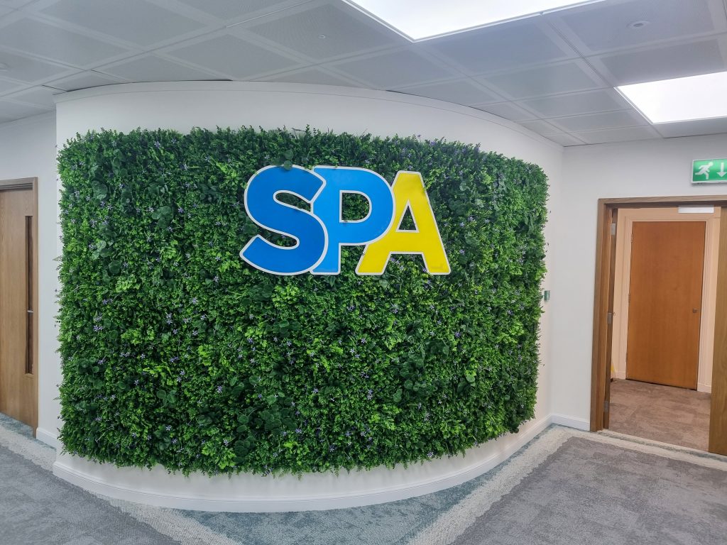 S.P.A blue and yellow letters fitted within a moss wall in an office space