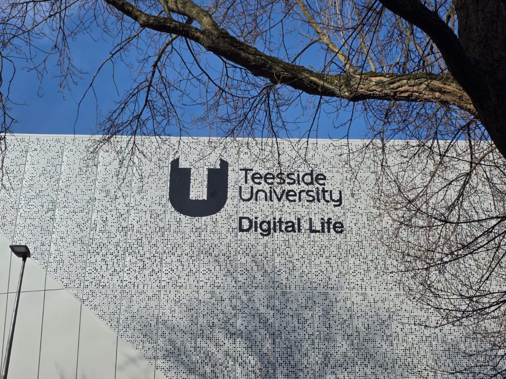 Teeside University black flat cut text and logo building sign fitted to perforated grey cladding